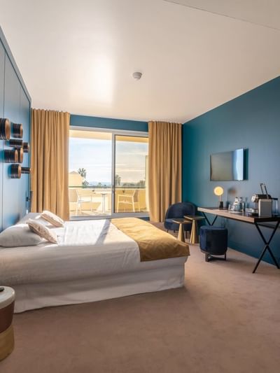 Chambre d'hôtel élégante avec lit, bureau, chaise, lampe, miroir, et porte-fenêtre avec vue.