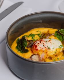 Poached egg with paprika atop creamy pumpkin purée, sautéed mushrooms, & microgreens in a dark bowl at Téséo Restaurant & Bar