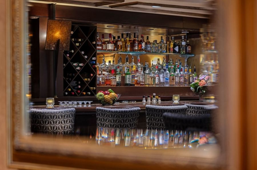 Margaux Lounge Bar featuring rows of liquor bottles by a wine rack under warm lighting at Warwick Seattle
