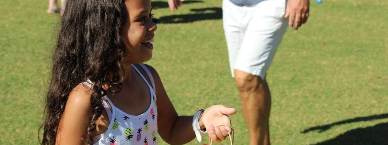 Child holding a bag of shiny Easter eggs surrounded by people on a grassy field at Novotel Sunshine Coast Resort