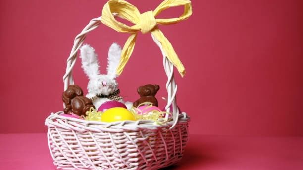 White Easter basket with chocolates, bunny, and egg on pink background for Events.
