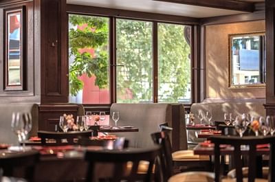Margaux Restaurant interior featuring booths by large windows overlooking green trees at Warwick Seattle