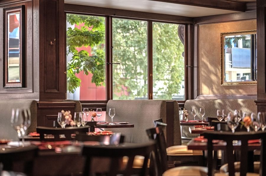 Margaux Restaurant interior featuring booths by large windows overlooking green trees at Warwick Seattle