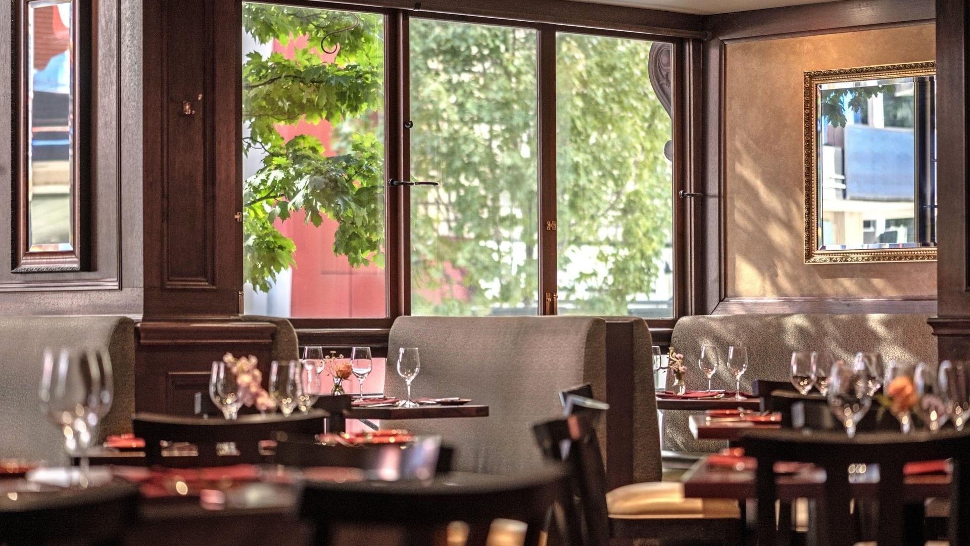 Margaux Restaurant interior featuring booths by large windows overlooking green trees at Warwick Seattle