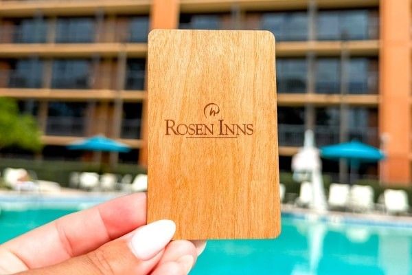 A close-up of a wooden Rosen Inns hotel room key in front of the pool and a room block at Rosen Inn Lake Buena Vista.