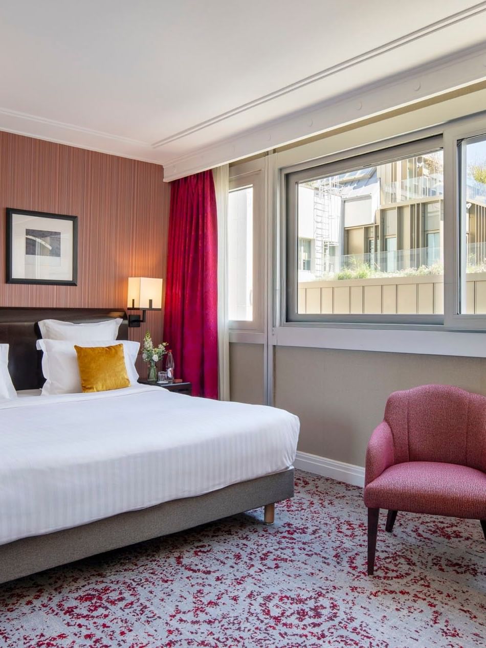 Deluxe Room features a modern bed with a pink armchair and side table under a large window at Warwick Paris Champs Elysées