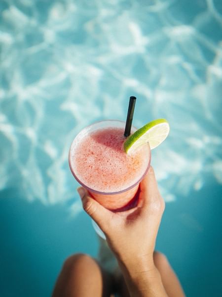 Frozen pink cocktail with a lime slice in hand by the pool at Warwick Melrose Dallas
