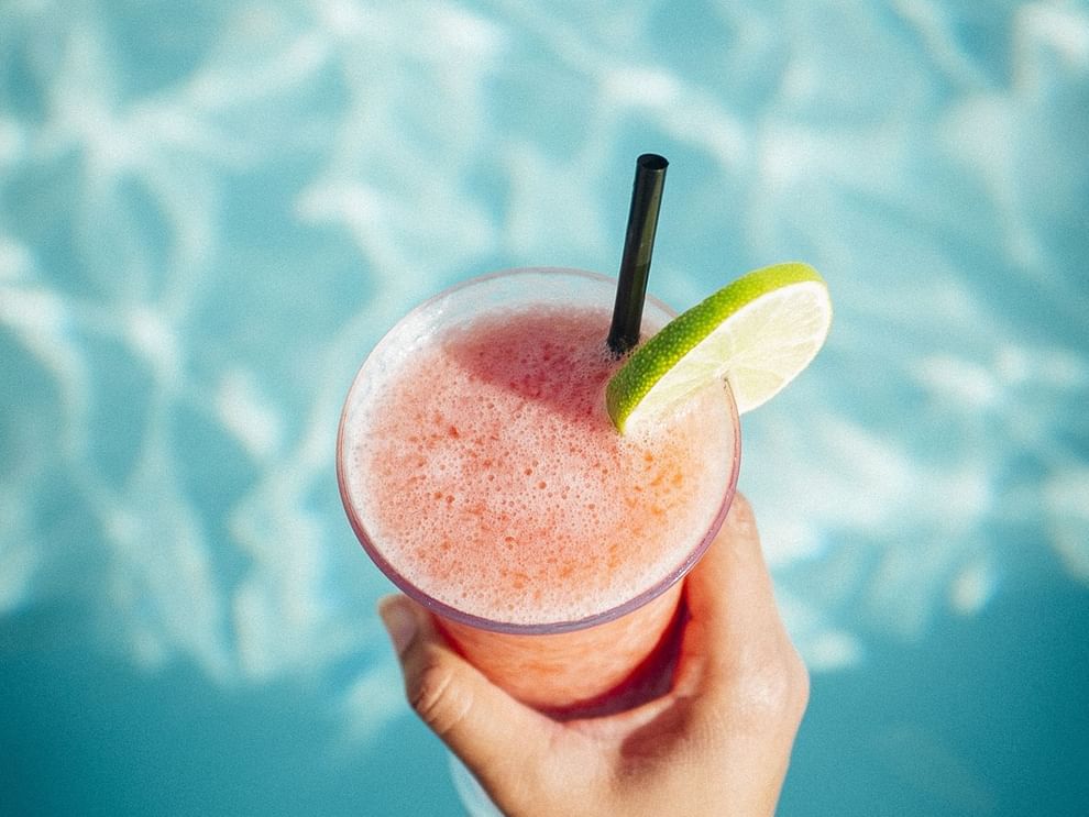 Frozen pink cocktail with a lime slice in hand by the pool at Warwick Melrose Dallas