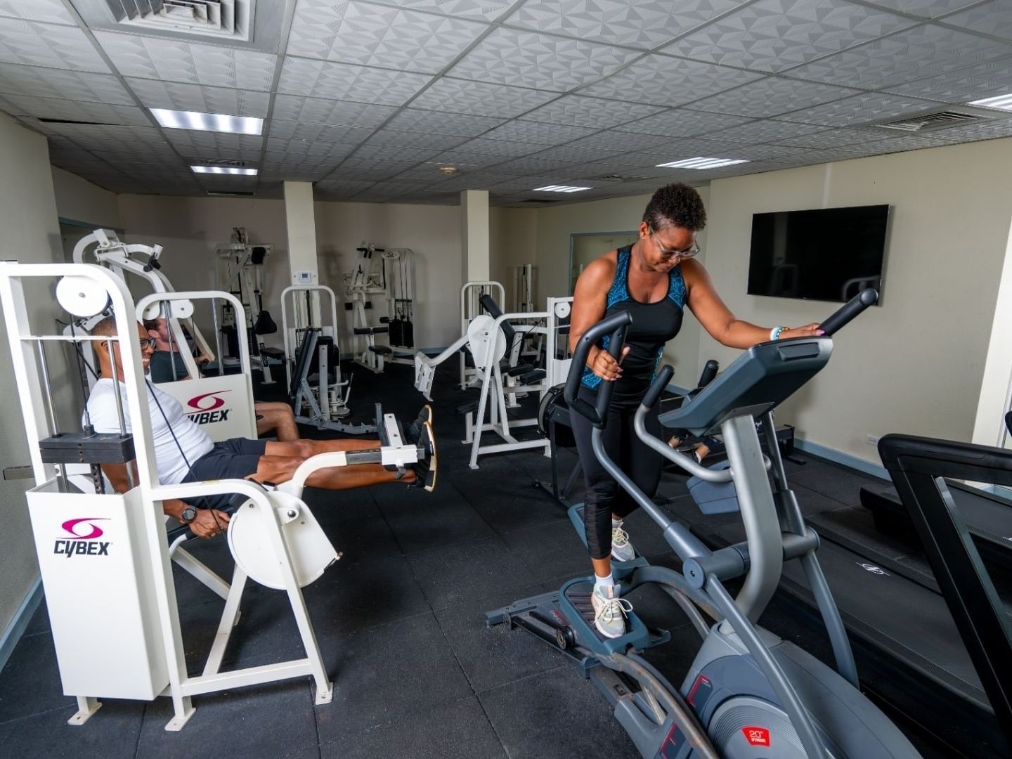 Two people using exercise machines in a gym.