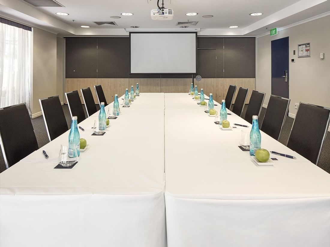 Boardroom with a long white table, executive chairs, water bottles, and a large presentation screen at The Sebel Brisbane