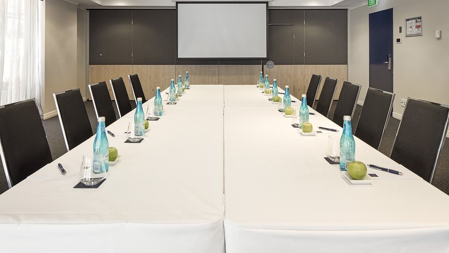Boardroom with a long white table, executive chairs, water bottles, and a large presentation screen at The Sebel Brisbane
