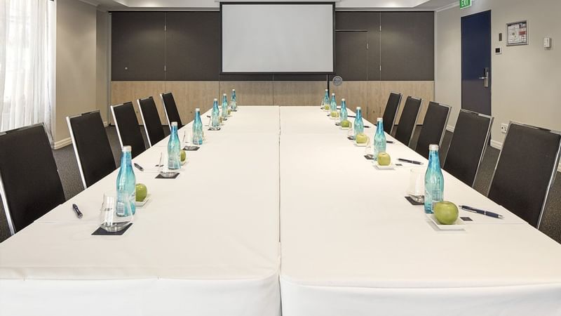 Boardroom with a long white table, executive chairs, water bottles, and a large presentation screen at The Sebel Brisbane