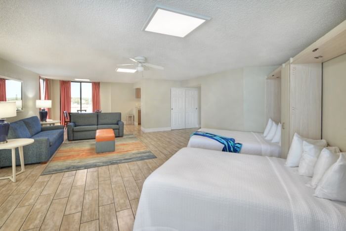 A wide view of a hotel suite with a seating area and two beds.