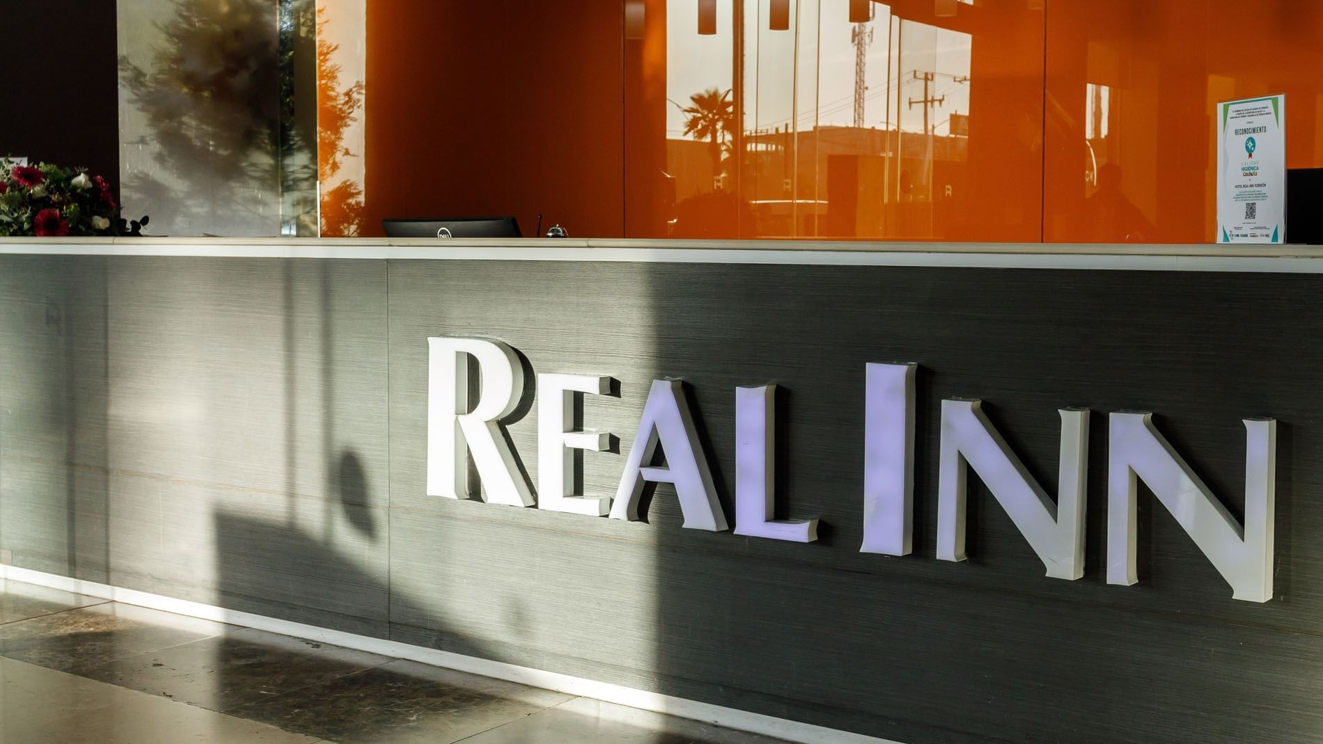 Close-up of the Real Inn Torreon logo on a textured grey reception desk, illuminated by soft ambient lighting