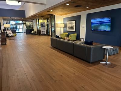 Lobby seating area with black sofas and green armchairs beneath a wooden ceiling near the entrance at Miami Lakes Hotel
