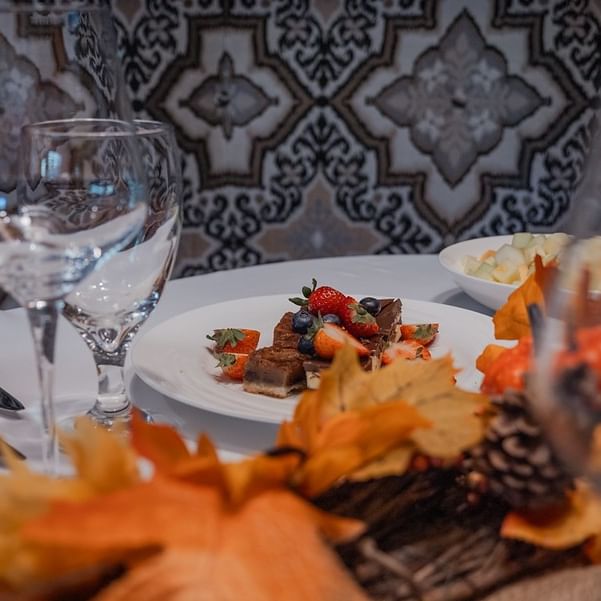 Elegantly plated dishes with autumn leaves and decorative elements on a table set for Thanksgiving Dinner.