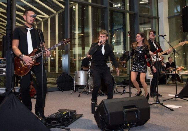 Live musical band performing on stage with singers and guitarists in front of floor to ceiling window at Hotel X Toronto