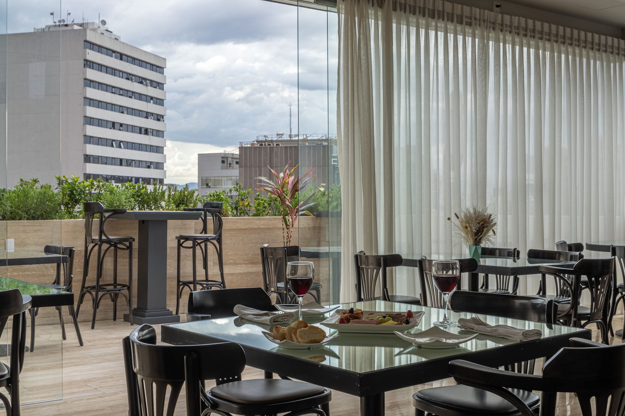 Elements by Marquis dining area with tables, chairs, and food, overlooking buildings through large windows.