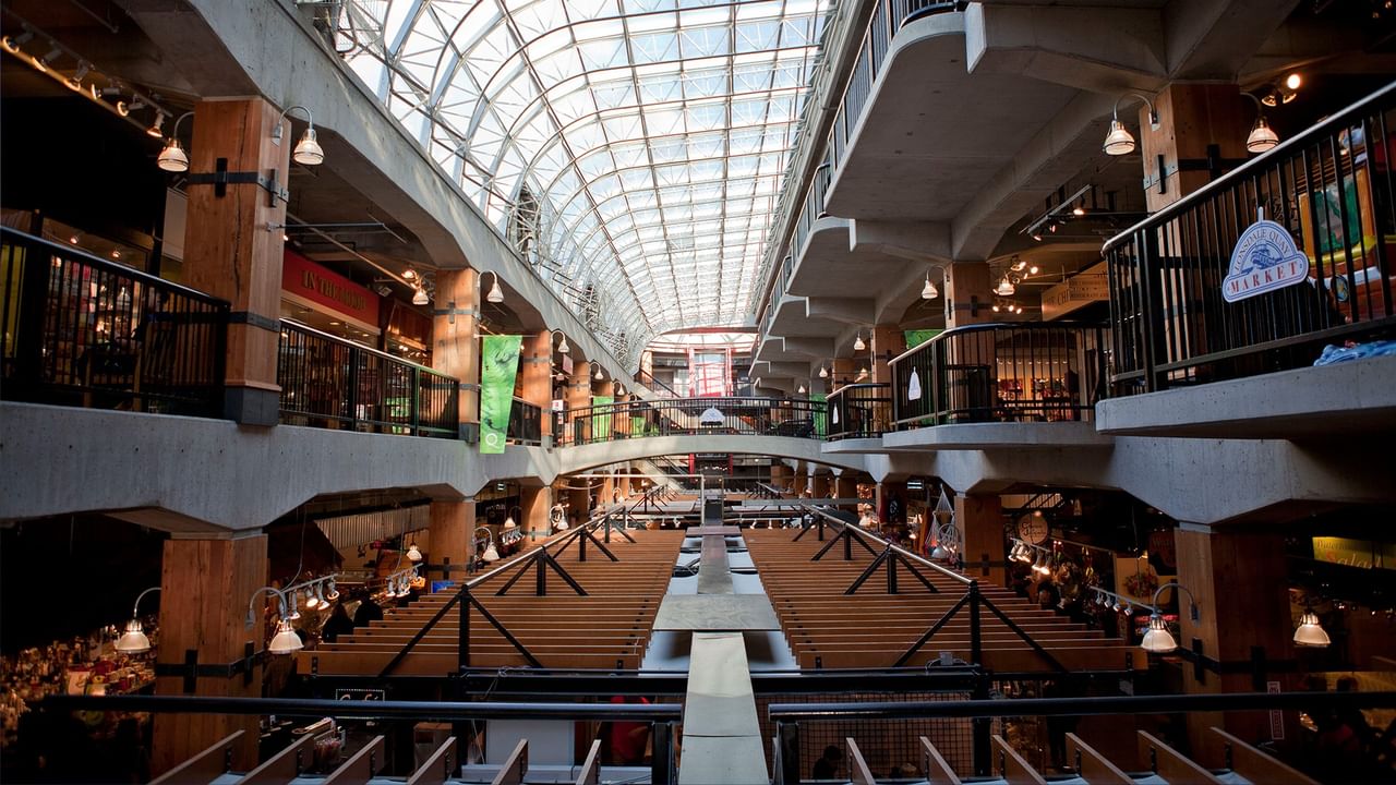 Interior of a shopping mall with a glass roof and various shops on two levels near Coast Lonsdale Quay Hotel