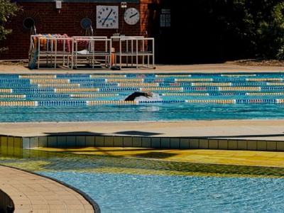 Swimmer doing the breast stroke in a public pool with lifeguard and clocks.