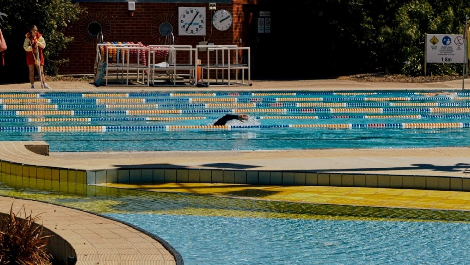 Swimmer doing the breast stroke in a public pool with lifeguard and clocks.
