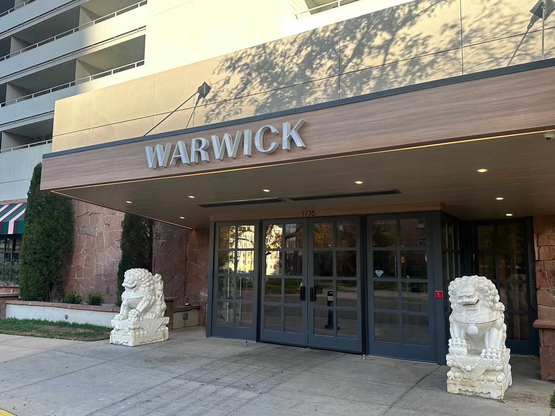 White stone lions guard the Warwick Denver entrance near the wooden awning and glass doors