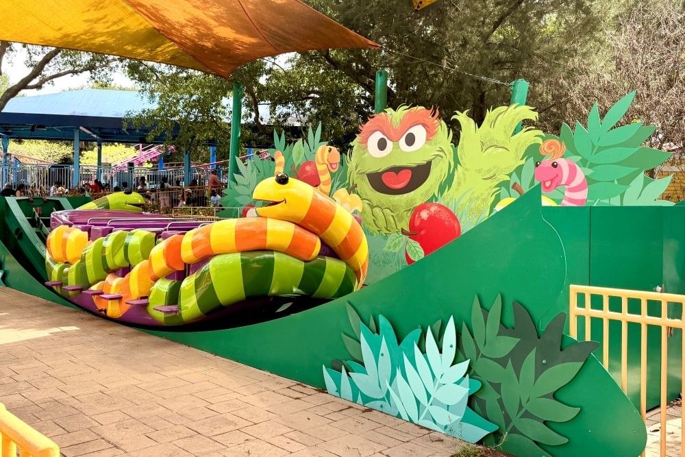 A children's ride with a figure of a smiling Oscar the Grouch and colorful striped ride cars at Sesame Street Land at SeaWorld Orlando.