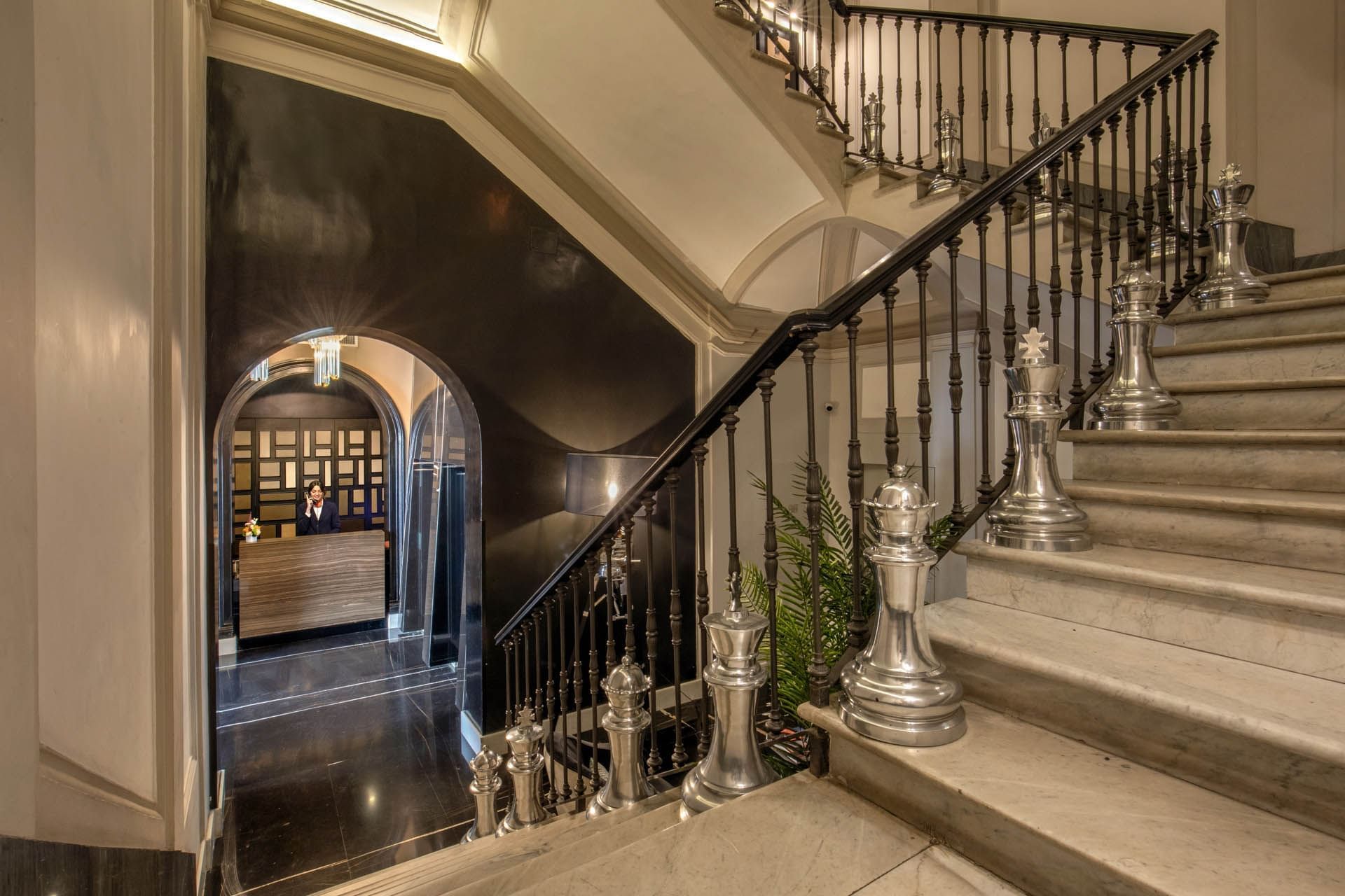 Staircase adorned with large silver chess pieces, leading to a reception area with decor at The Glam Hotel