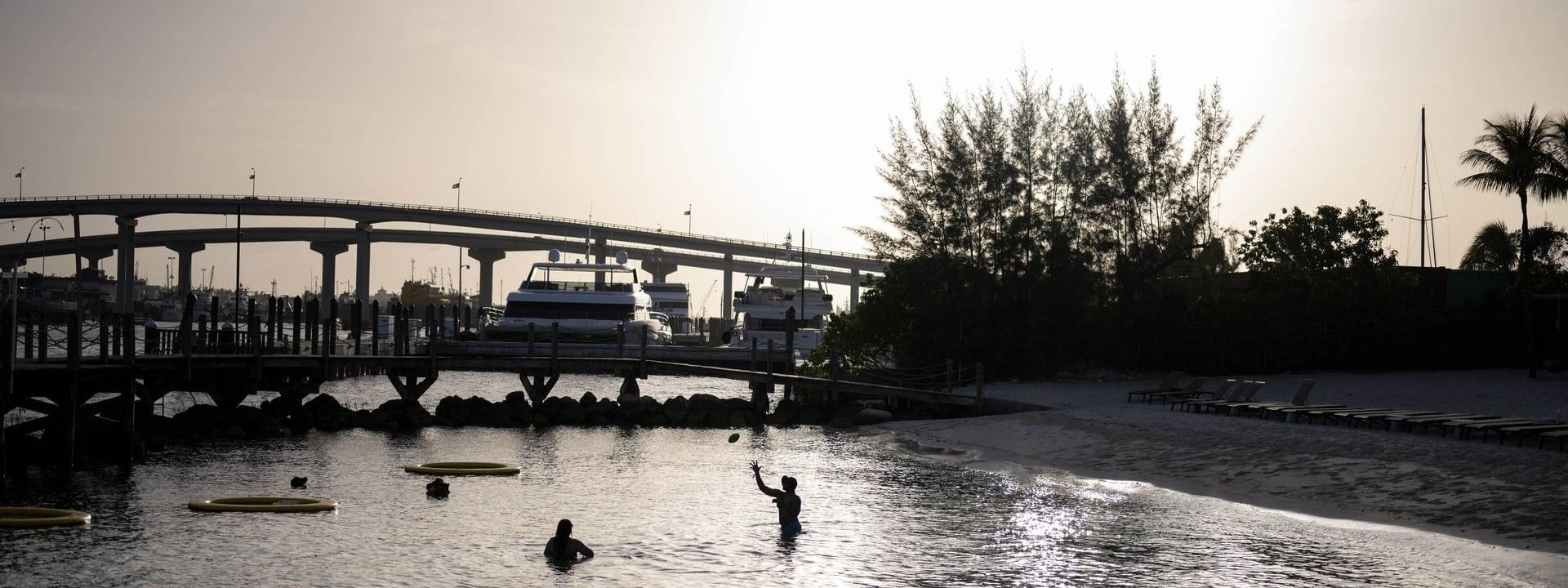 Silhouetted guests in water by a harbor under a glowing sunset near a bridge at Warwick Paradise Island Bahamas