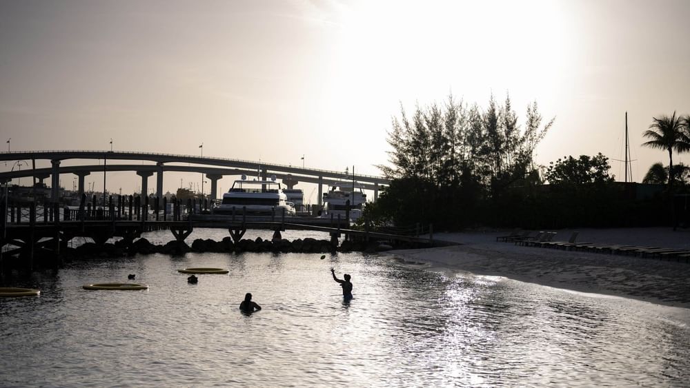 Silhouetted guests in water by a harbor under a glowing sunset near a bridge at Warwick Paradise Island Bahamas