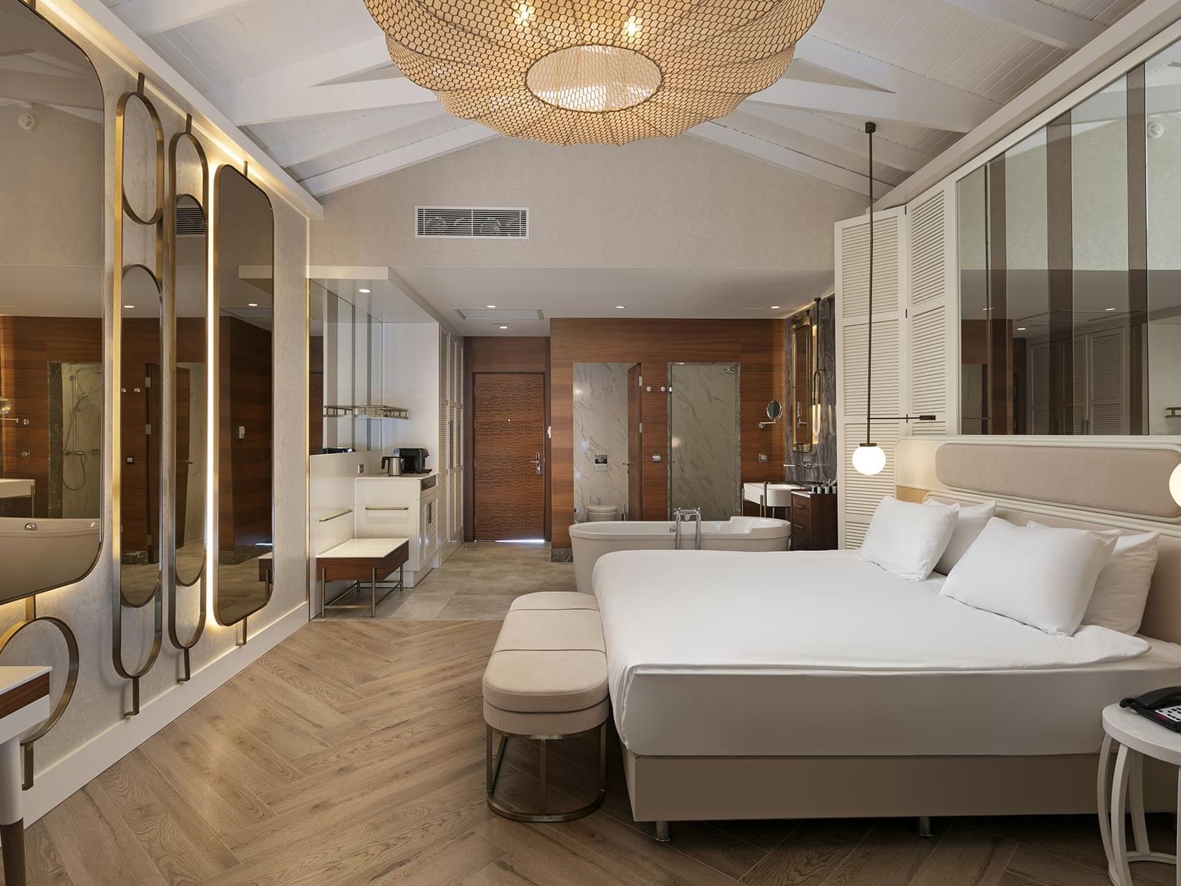 Spacious modern hotel suite with king bed, herringbone floors, gold-accented mirrors, and glass-enclosed bathroom at Titanic Deluxe Golf Belek