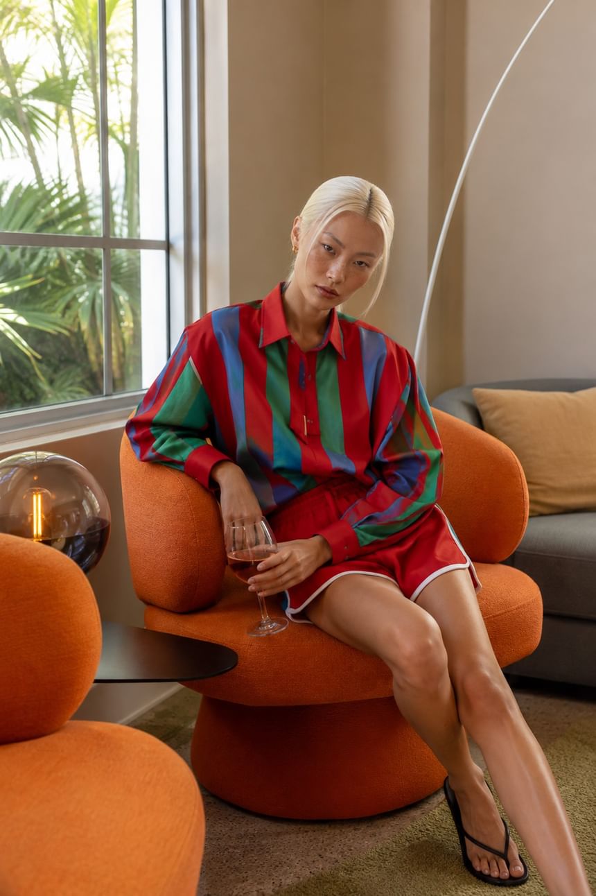 Guest relaxing in orange modern chair with wine glass near window with tropical plants at Kenmore Village Hotel, South Beach