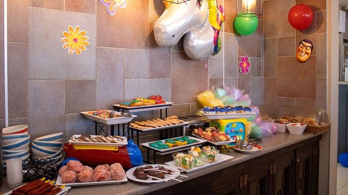 Colorful children\'s dessert buffet with cakes and treats beneath festive balloons in Palmira Cafeteria at Araiza Calafia