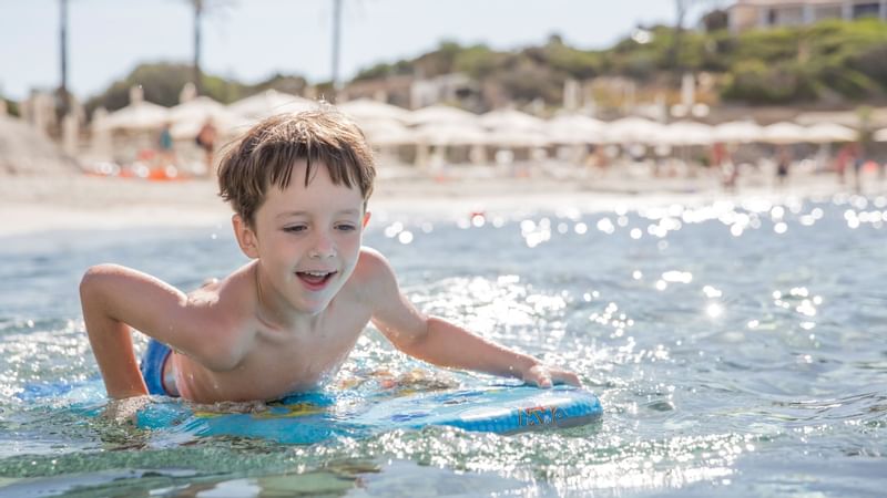 Small boy on a surf board in the sea near Falkensteiner Hotels