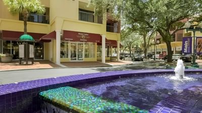 Miami Lakes Jewelers storefront beside shaded sidewalk and purple tiled fountain along Main St near Miami Lakes Hotel