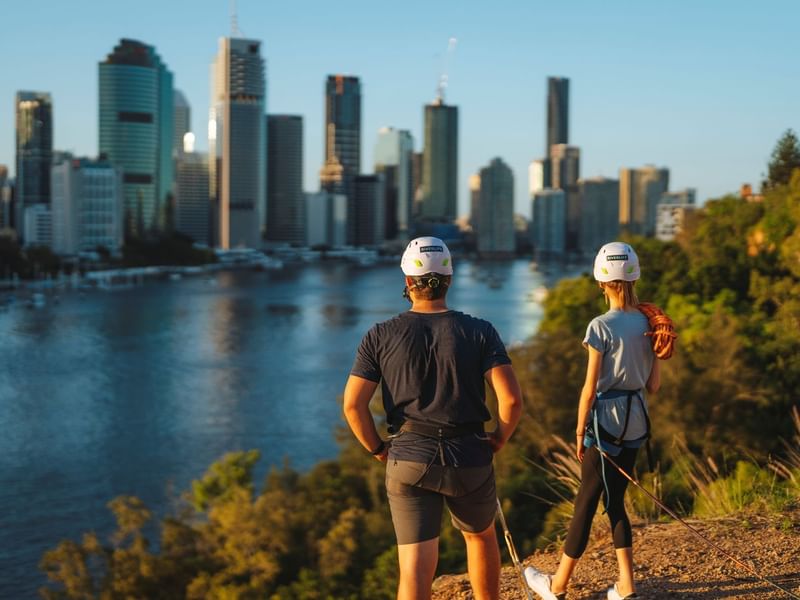 Two people wearing helmets overlooking a river with city skyline at Kangaroo Point near Sofitel Brisbane Central