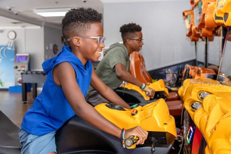 Two boys wearing glasses play racing arcade games on yellow motorcycle simulators at Legacy Vacation Resorts
