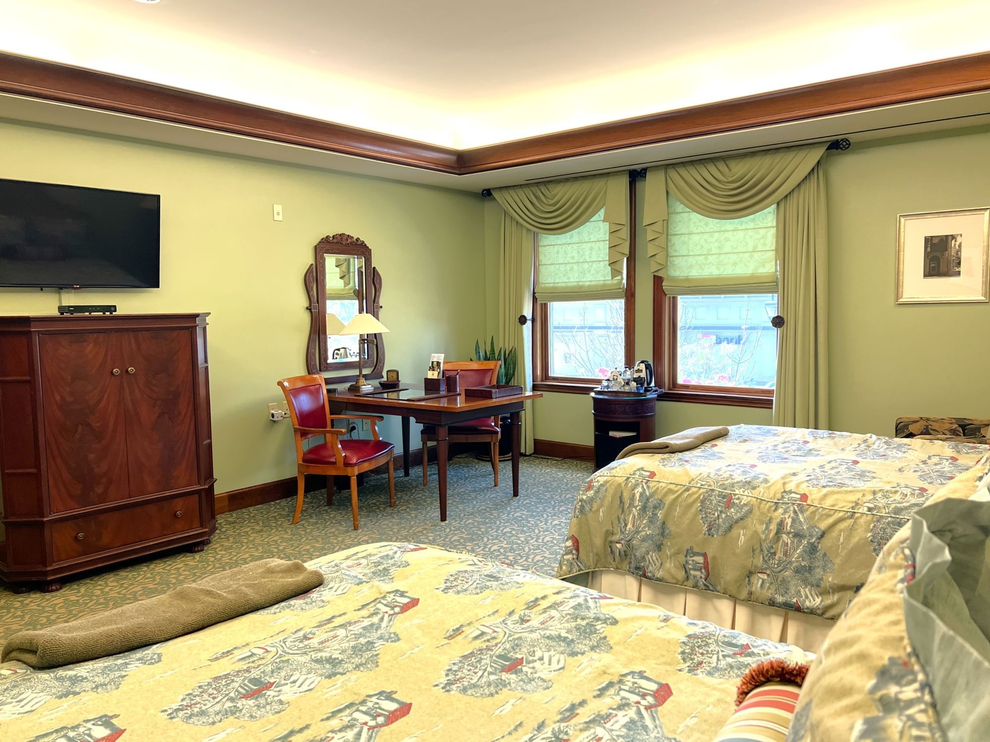 Deluxe Double Queen room with two beds, a wooden dresser, a modern TV, and a desk with chairs at The Rose Hotel
