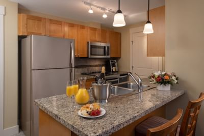Modern kitchen with granite counter, breakfast plate, wine, flowers, and two chairs next to a bar.