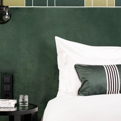 Letto con cuscino verde e bianco, bicchiere, libri, e lampada a sospensione in camera.
