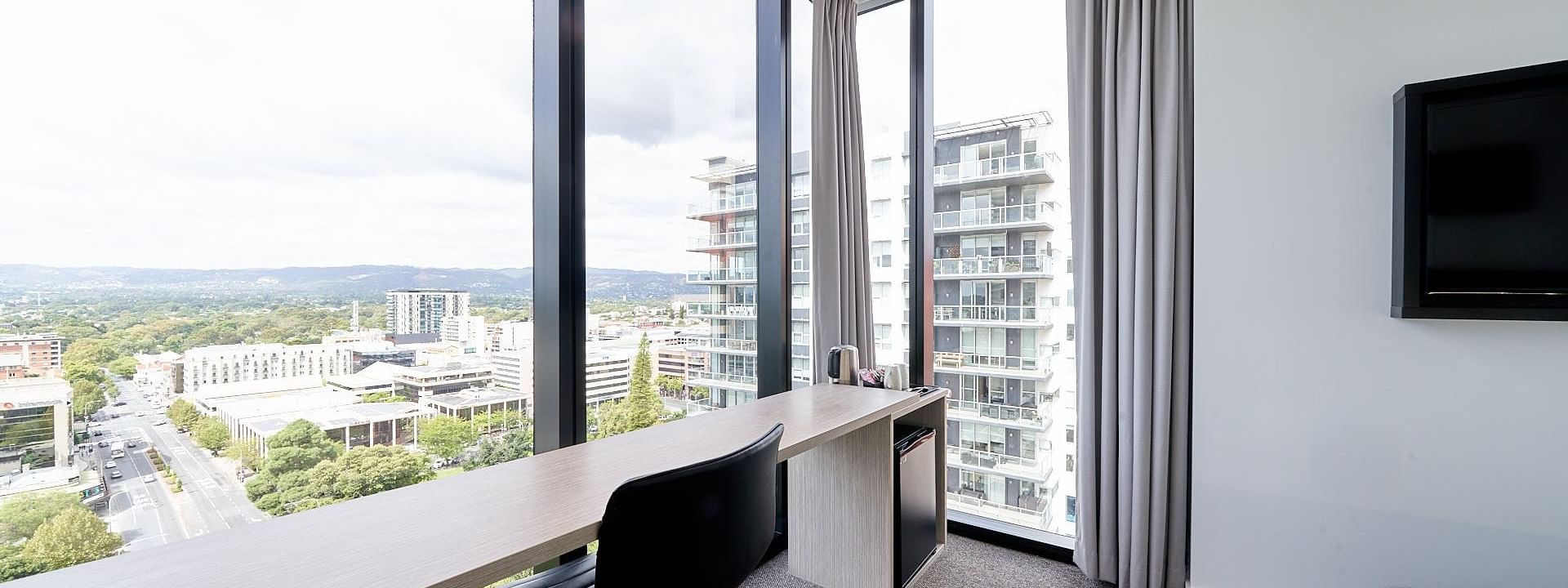 Deluxe Corner Room One Queen Bed featuring a large work desk by the window with Panoramic city views at Ibis Adelaide