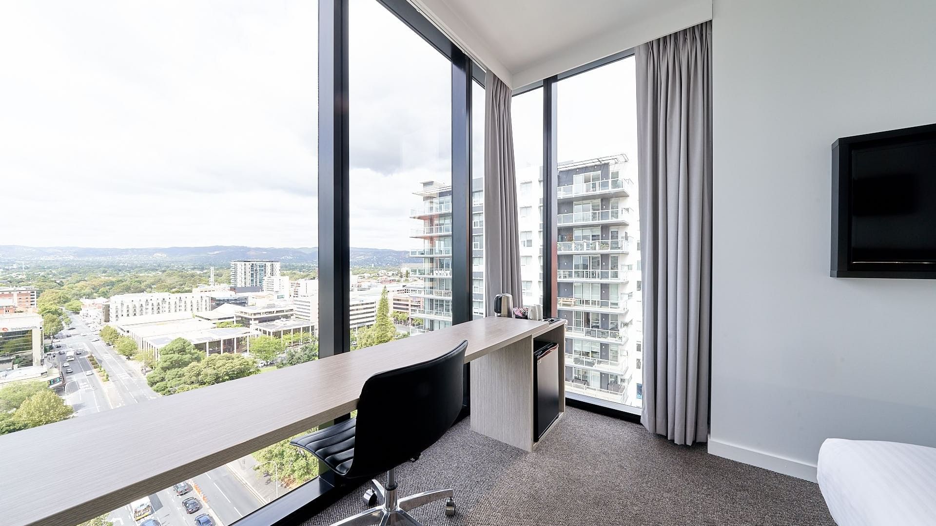 Deluxe Corner Room One Queen Bed featuring a large work desk by the window with Panoramic city views at Ibis Adelaide