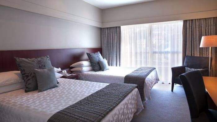 Twin king bed, working desk with an armchair in a bedroom at James Cook Hotel Grand Chancellor