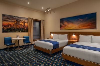 Two queen beds with a city art above the headboard and a table near a window in Double Queen Atrium at Harborside Inn Boston