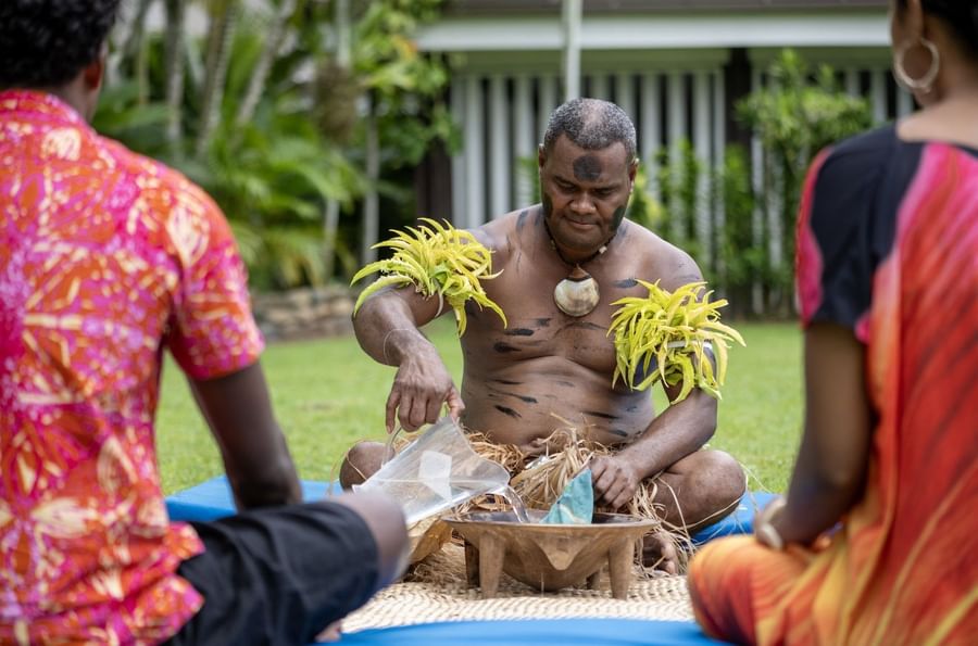Traditional performer pouring water into a bowl on a mat surrounded by guests at Tambua Sands Beach Resort
