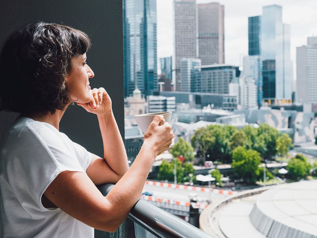 Lady drinking tea on the balcony in 1 Bedroom Deluxe Apartment at Quay West Suites Melbourne