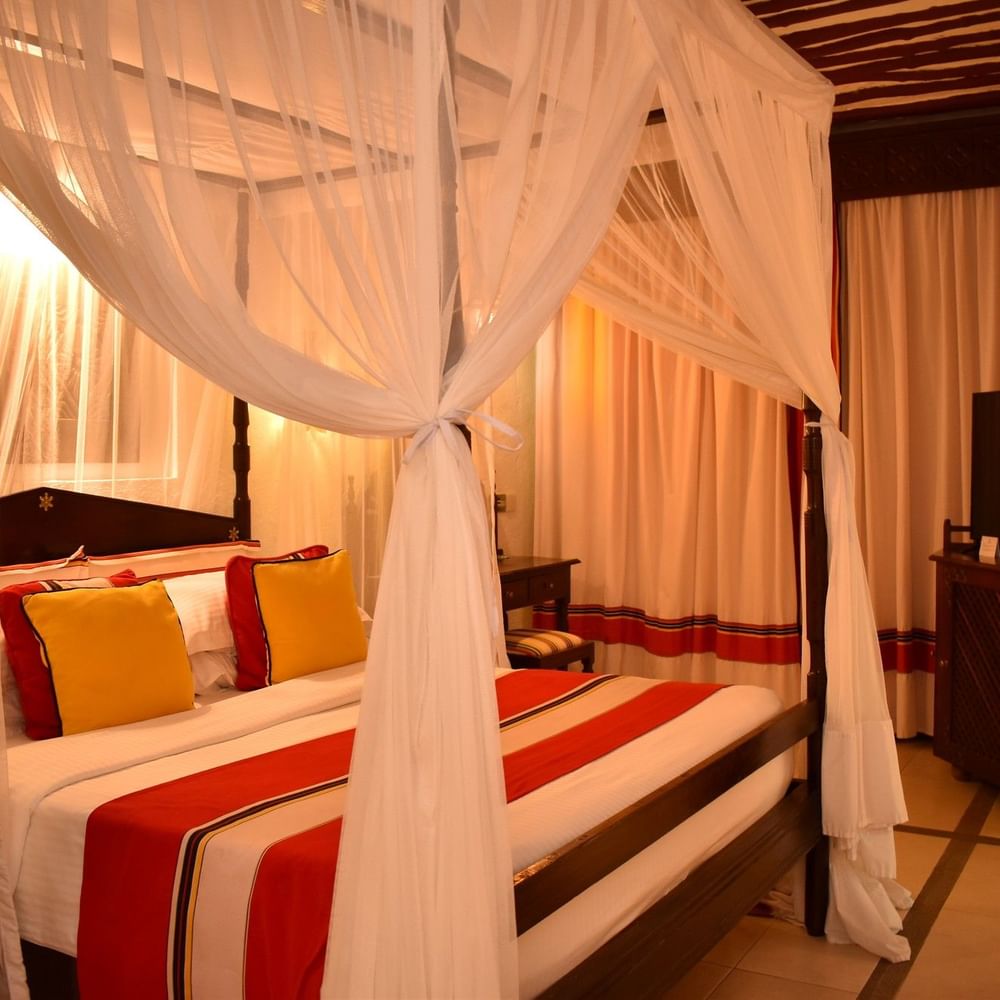 Zanzibar Suite with a canopy bed, curtains, and a TV at Serena Beach Resort & Spa, Mombasa.
