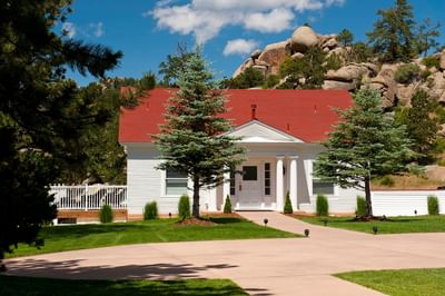 Presidential Cottage with a red roof at The Stanley Hotel, with a manicured lawn, pine trees, and a mountain backdrop