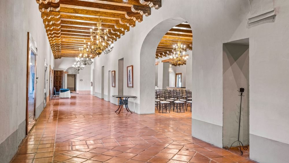 Long tiled corridor with white arches, gold chandeliers, and wood beams in La Concepción at Quinta Real Puebla