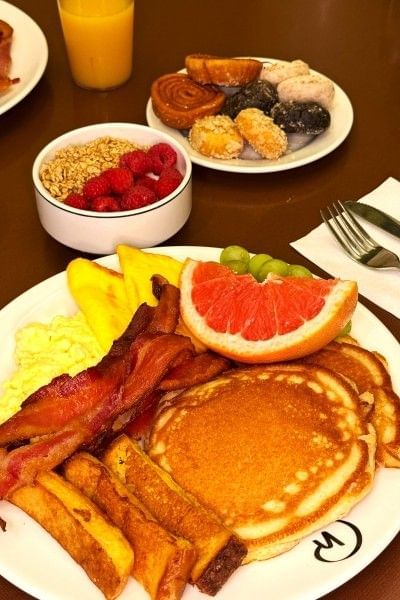Plates of breakfast foods including pancakes, yogurt, pastries, bacon, and eggs at the buffet at Rosen Inn.